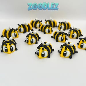 May include: A collection of yellow and black bee-shaped figurines with white accents. The figurines have large, cartoonish eyes and small white antennae. The word "Zoodlez" is displayed in blue above the figurines.
