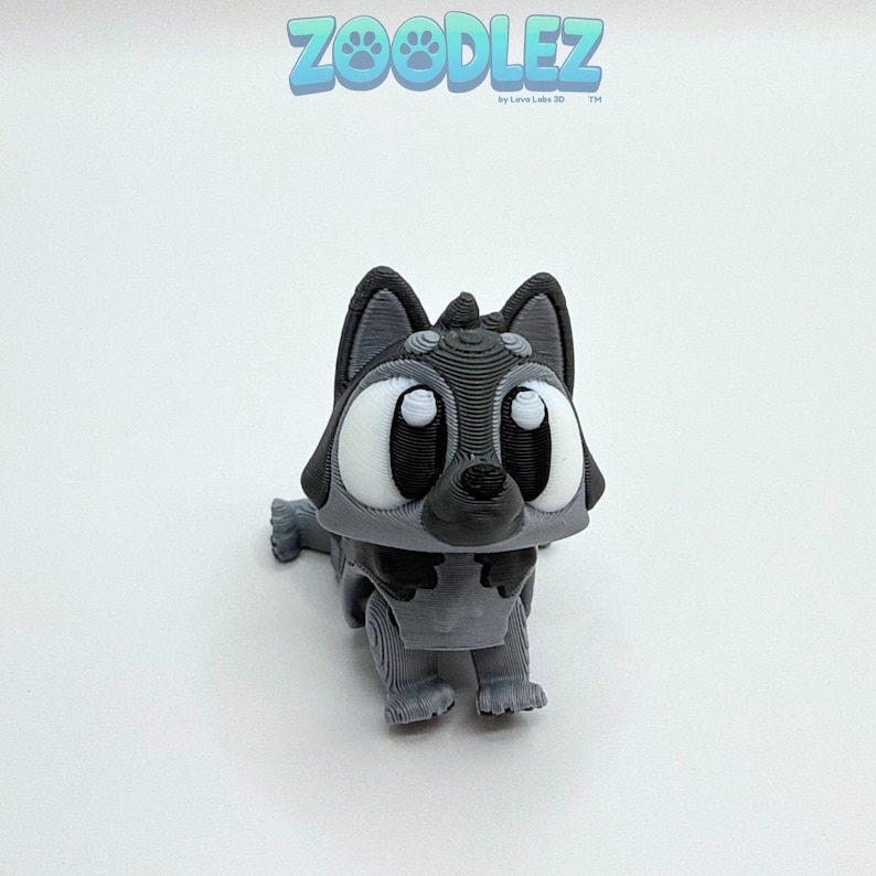 May include: A 3D-printed gray and black cartoon wolf figurine with large white eyes. The figurine is in a crouching position. The word "Zoodlez" is printed in blue above the figurine.