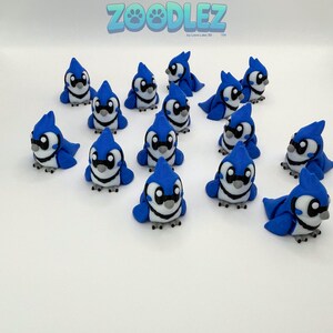 May include: A collection of blue jay figurines with white and black accents. The figurines are in various poses, some standing and others sitting. The word "Zoodlez" is visible in the top center of the image.