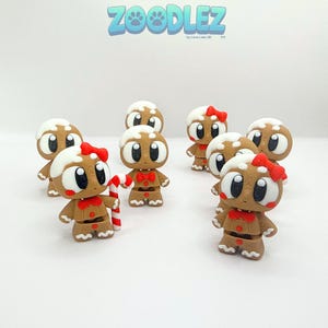 May include: Several gingerbread man figurines with white icing, red bowties, and red bows. One holds a candy cane. The Zoodlez logo is at the top. These festive decorations are perfect for the holiday season.