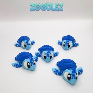 May include: Five blue turtle figurines with light blue details and large, expressive eyes are arranged on a white surface. The turtles have textured shells and flipper-like appendages. The word "Zoodlez" is at the top.