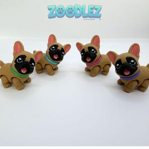 May include: Four tan French bulldog figurines with black faces and pink tongues. Each dog wears a different colored collar: green, light blue, pink, or purple. The text ZOODLEZ by Love Labs 3D is printed in blue at the top of the image.