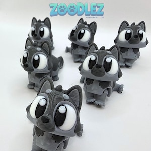 May include: A collection of gray and white 3D-printed wolf figurines with large, expressive eyes. The figurines have a cartoonish design and are arranged on a white surface. The word "Zoodlez" is displayed in blue text at the top.