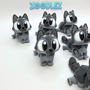 May include: Several gray and black 3D-printed wolf figurines with large white eyes and the text "ZOOODLEZ" in blue and green. The figurines are in various poses, with some standing and others lying down.