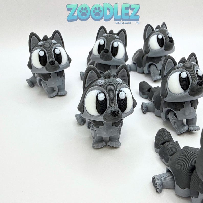 May include: Several gray and black 3D-printed wolf figurines with large white eyes and the text "ZOOODLEZ" in blue and green. The figurines are in various poses, with some standing and others lying down.
