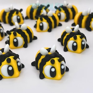 May include: A collection of small, three-dimensional bee figurines featuring bright yellow bodies with bold black stripes, large white eyes with black pupils, and small white wings. Each bee has a rounded shape and a smooth, layered texture.