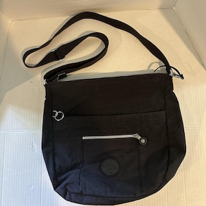 May include: Black crossbody bag with a long adjustable strap. The bag has a front zippered pocket and a small round logo. The bag is made of a durable, water-resistant material.