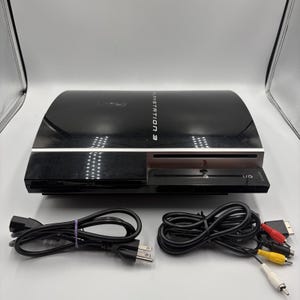 May include: A black PlayStation 3 game console with a glossy finish, featuring the text PLAYSTATION 3 on the top surface. The console is accompanied by a black power cord and a multi-colored AV cable with red, yellow, and white RCA connectors.