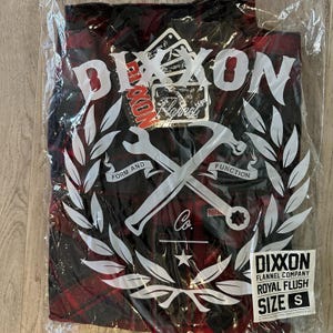 May include: A red and black plaid flannel shirt in a plastic bag. The shirt has a white graphic with the word "DIXON" and the words "FORM AND FUNCTION". The shirt is size small.