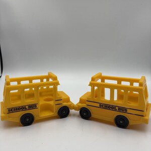 May include: Two yellow toy school buses with black wheels. Each bus has the words "SCHOOL BUS" printed on the side. The buses are made of plastic and have a simple, open-top design.