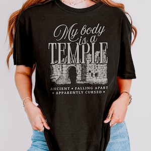 May include: Black t-shirt with the text "My body is a TEMPLE" in a stylized font above an illustration of a stone structure. Below the illustration are the words "ANCIENT - FALLING APART - APPARENTLY CURSED".