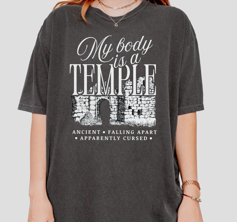 May include: A black t-shirt with a white graphic that reads 'My body is a TEMPLE' with a drawing of a crumbling stone building below. The text below the drawing reads 'ANCIENT - FALLING APART - APPARENTLY CURSED'.