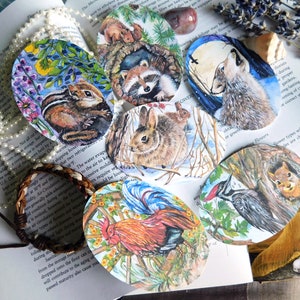May include: A collection of oval-shaped watercolor paintings featuring various woodland animals. The paintings depict a chipmunk, raccoon, rabbit, wolf, squirrel, rooster, and woodpecker. Each painting showcases detailed illustrations of the animals in their natural habitats, with vibrant colors.