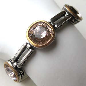 May include: A bracelet featuring three square-shaped, light champagne-colored faceted crystals set in gold-toned bezels. The links connecting the crystals are made of oxidized silver-toned metal with intricate scrollwork patterns on the sides.