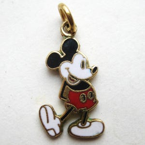 Puede incluir: Un charm de Mickey Mouse dorado con orejas negras, cara blanca y pantalones cortos rojos. El charm tiene un lazo dorado para sujetarlo a una pulsera o collar. El ic&oacute;nico personaje de dibujos animados se representa caminando.
