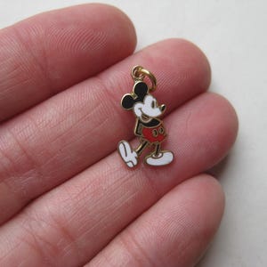 Puede incluir: Un peque&ntilde;o dije de Mickey Mouse de color dorado. El dije presenta una cabeza y orejas negras, una cara blanca, pantalones cortos rojos y guantes y zapatos blancos. El dije est&aacute; unido a un peque&ntilde;o lazo dorado.