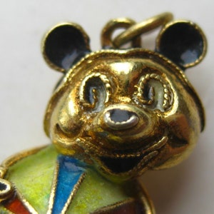 May include: A gold-toned metal pendant shaped like a bear with black enamel ears and nose. The bear features a colorful body with segments of yellow, blue, and red enamel. A small metal loop is attached to the top of the bear's head for hanging.