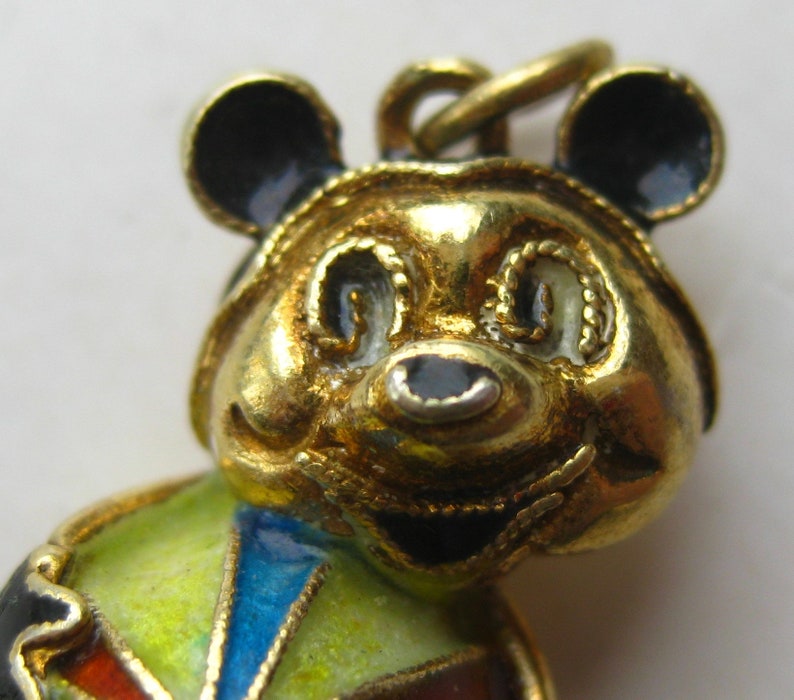 May include: A gold-toned metal pendant shaped like a bear with black enamel ears and nose. The bear features a colorful body with segments of yellow, blue, and red enamel. A small metal loop is attached to the top of the bear's head for hanging.