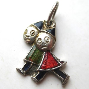 May include: A vintage silver charm featuring two stylized figures. The figures wear colorful outfits with red, green, and blue accents. The charm has a loop at the top for attachment to a bracelet or necklace. The charm is a unique piece of jewelry.