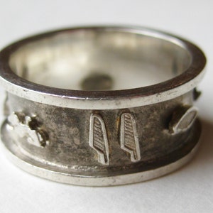 May include: A silver ring with a detailed band. The band features embossed designs, including what appear to be stylized feathers. The ring has a worn, vintage appearance.