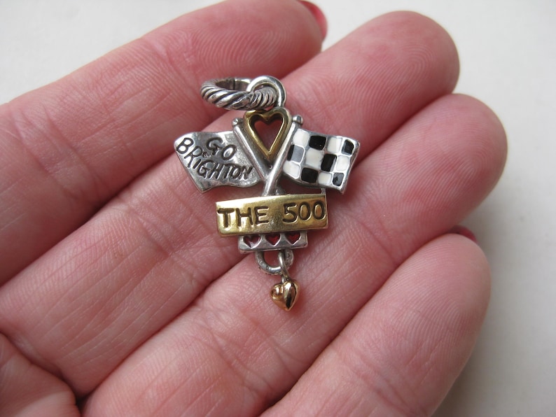 May include: Silver and gold-toned charm with a racing theme. Features two crossed flags, one checkered and one with text "GO BRIGHTON". The charm includes the text "THE 500" and a small heart pendant.