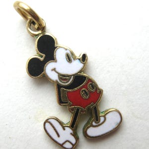 Puede incluir: Un charm de Mickey Mouse en tono dorado. El charm presenta a Mickey en su pose cl&aacute;sica, con cara blanca, orejas negras, pantalones cortos rojos y guantes y zapatos blancos. Tiene un lazo en la parte superior para sujetarlo a un collar o pulsera.