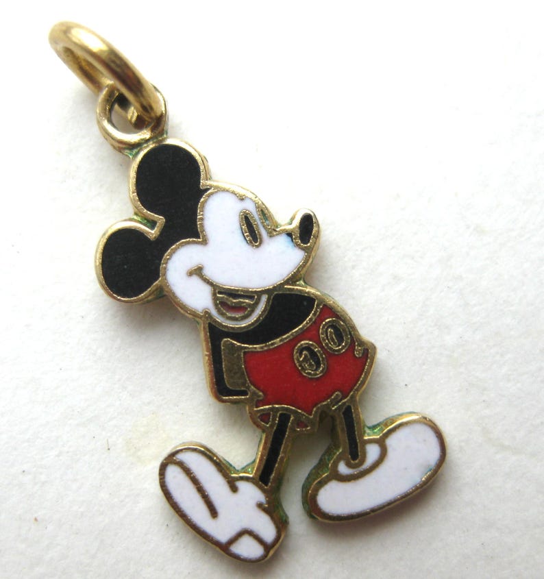 Puede incluir: Un charm de Mickey Mouse en tono dorado. El charm presenta a Mickey en su pose cl&aacute;sica, con cara blanca, orejas negras, pantalones cortos rojos y guantes y zapatos blancos. Tiene un lazo en la parte superior para sujetarlo a un collar o pulsera.