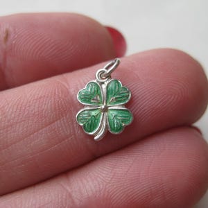 K&ouml;nnte beinhalten: Ein kleiner, silberfarbener Anh&auml;nger in Form eines vierbl&auml;ttrigen Kleeblatts. Die Bl&auml;tter des Kleeblatts sind mit gr&uuml;ner Emaille verziert, und der Anh&auml;nger hat eine kleine Schlaufe zum Befestigen an einer Halskette oder einem Armband. Ein Gl&uuml;ckssymbol.