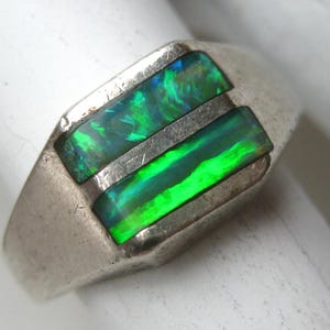 May include: A silver ring featuring two rectangular, horizontally set inlay stones with vibrant green and blue iridescent flashes. The metal band has a smooth, polished finish and a wide, flat top section that holds the two distinct gemstone inlays.