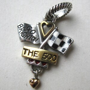 May include: A silver and gold charm with a racing theme. Features two flags, one checkered and one with the text "Go Brighton". The charm also includes the text "THE 500" and a small heart pendant.