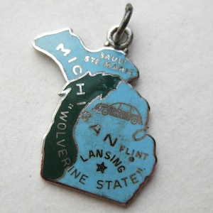 Peut inclure: Un pendentif en métal argenté en forme de l'État du Michigan, avec un émail bleu clair et vert foncé. Le bijou porte les inscriptions MICHIGAN, SAULT STE MARIE, FLINT, LANSING et WOLVERINE STATE, ainsi qu'un petit motif de voiture gravé.