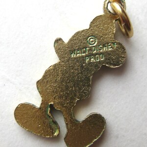 Puede incluir: Un charm de Mickey Mouse de color dorado con un lazo para sujetarlo a una pulsera o collar. El charm tiene el texto "WALT DISNEY PROD" en la parte posterior. El charm tiene la forma de Mickey Mouse.
