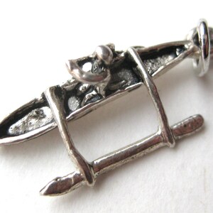 May include: A silver-colored charm in the shape of a kayak. The charm has a detailed design with a loop at one end for attaching to a bracelet or necklace. The kayak charm is a miniature representation of a watercraft.