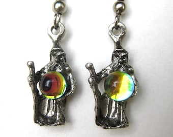May include: A pair of silver-toned wizard earrings. Each earring features a detailed wizard figure holding a colorful, iridescent orb. The wizards have long beards and are holding a staff. The orbs have a mix of yellow, red, and green hues.