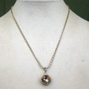 Puede incluir: Un collar con una cadena de dos tonos con cuentas alternas de color dorado y plateado. El colgante es un cristal redondo facetado de color champ&aacute;n engastado en un bisel de metal dorado, suspendido de una anilla de metal plateado.