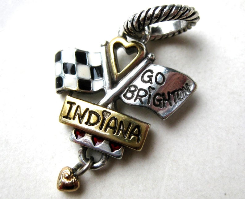 May include: A silver and gold charm with a racing theme. Features a checkered flag, a flag that says "GO BRIGHTON", and a banner that says "INDIANA". Includes a heart-shaped charm and a twisted silver ring.