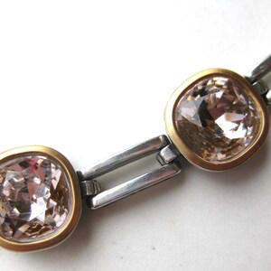 May include: A bracelet featuring a series of square-shaped, light champagne-colored faceted crystals. Each crystal is set within a smooth, matte gold-toned bezel, connected by polished silver-toned rectangular metal links in a chain design.