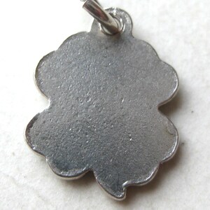 K&ouml;nnte beinhalten: Ein silberfarbener Anh&auml;nger in Form eines vierbl&auml;ttrigen Kleeblatts. Der Anh&auml;nger hat eine strukturierte Oberfl&auml;che und eine kleine Schlaufe oben zum Befestigen an einer Kette oder einem Armband. Das Kleeblatt-Design ist ein klassisches Symbol f&uuml;r Gl&uuml;ck und Wohlstand.