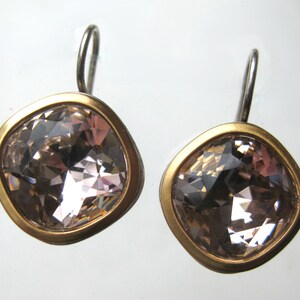 May include: A pair of earrings featuring square-shaped, faceted light pink crystals set in smooth, matte gold-toned metal bezels. Each earring is attached to a simple, curved silver-toned metal ear wire hook for hanging, showcasing a clean design.