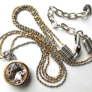 Puede incluir: Un collar de varias cadenas con un gran colgante de cristal facetado de color rosa p&aacute;lido y forma cuadrada, engastado en un bisel dorado. La cadena presenta eslabones de cuentas alternos en plata y oro, con un cierre de mosquet&oacute;n plateado.