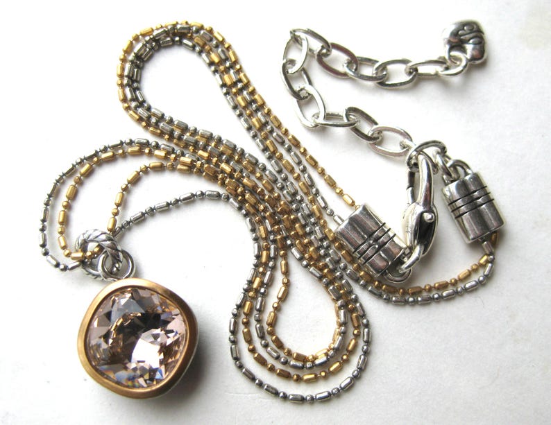 Puede incluir: Un collar de varias cadenas con un gran colgante de cristal facetado de color rosa p&aacute;lido y forma cuadrada, engastado en un bisel dorado. La cadena presenta eslabones de cuentas alternos en plata y oro, con un cierre de mosquet&oacute;n plateado.