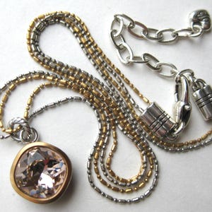 Puede incluir: Un collar de varias cadenas con cuentas en tonos oro y plata. El colgante es un cristal rosa claro facetado de forma cuadrada engastado en un bisel dorado. El collar incluye un cierre de mosquet&oacute;n plateado y una cadena de extensi&oacute;n.
