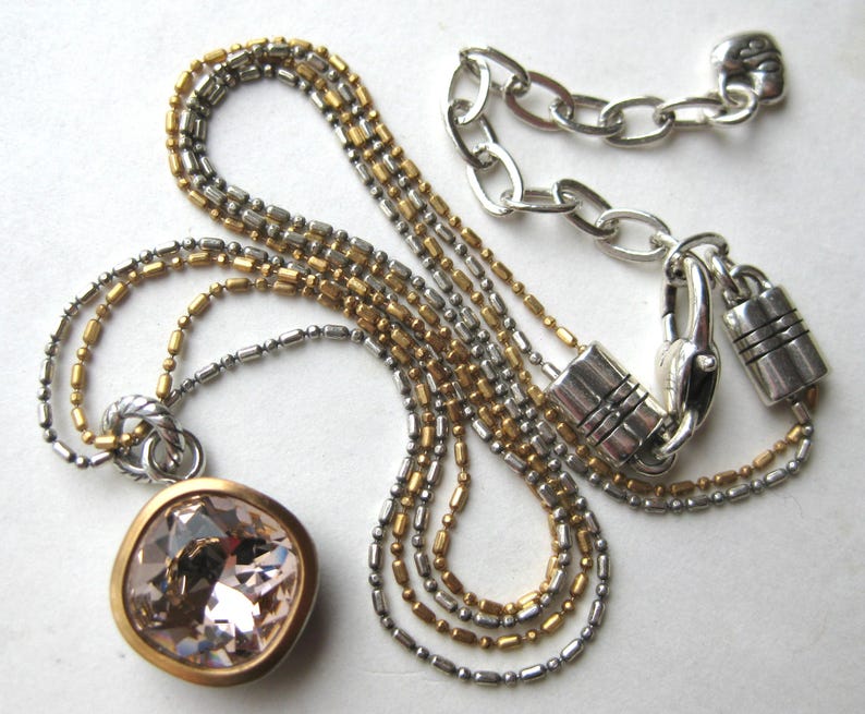 Puede incluir: Un collar de varias cadenas con cuentas en tonos oro y plata. El colgante es un cristal rosa claro facetado de forma cuadrada engastado en un bisel dorado. El collar incluye un cierre de mosquet&oacute;n plateado y una cadena de extensi&oacute;n.