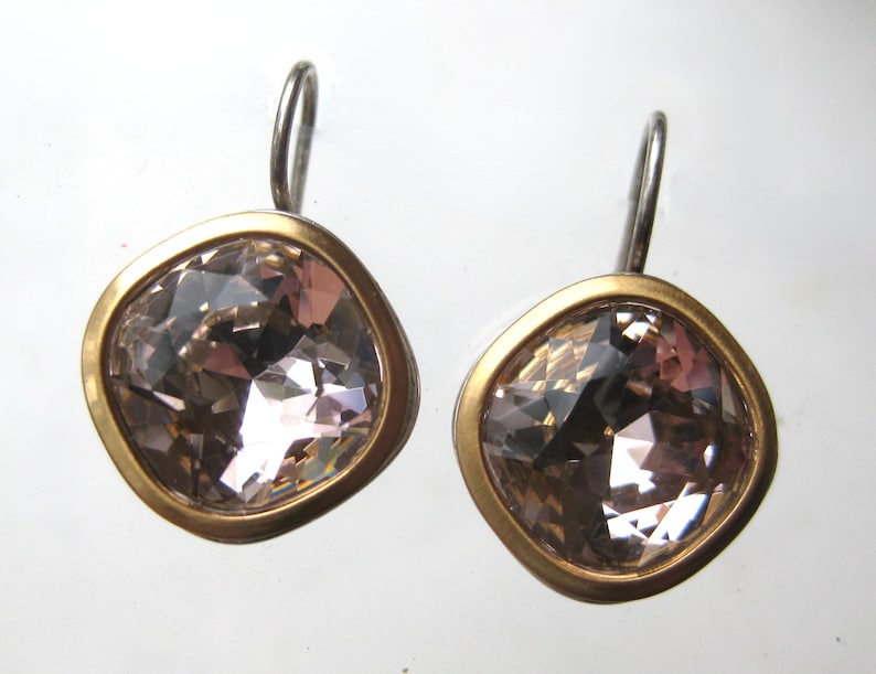 May include: A pair of drop earrings featuring square-shaped, faceted champagne-colored crystals set in smooth, matte gold-toned metal bezels. Each earring is attached to a simple, curved silver-toned metal hook for secure placement on the ear.
