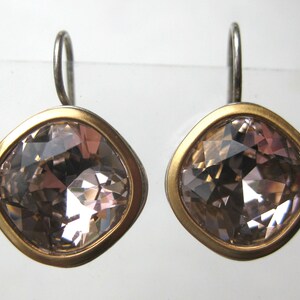 May include: A pair of earrings featuring square-shaped, faceted light brown crystals set in a smooth gold-toned metal bezel. Each earring is attached to a simple silver-toned metal hook wire, providing a secure and balanced look for the jewelry.