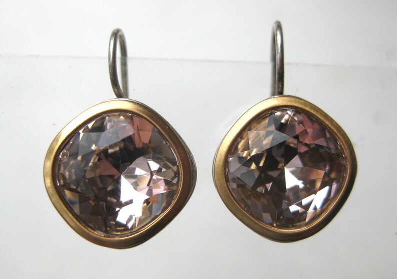 May include: A pair of earrings featuring square-shaped, faceted light brown crystals set in a smooth gold-toned metal bezel. Each earring is attached to a simple silver-toned metal hook wire, providing a secure and balanced look for the jewelry.