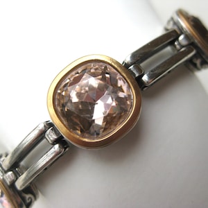 May include: A link bracelet featuring square-shaped, faceted light pink stones set in gold-toned bezels. The stones are connected by polished silver-toned metal links with decorative scrollwork details on the sides of each stone setting.