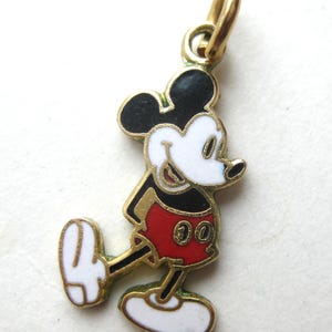 Puede incluir: Un charm de Mickey Mouse dorado con orejas negras, cara blanca y pantalones cortos rojos. El charm tiene un peque&ntilde;o lazo en la parte superior para sujetarlo. El personaje de dibujos animados cl&aacute;sico se representa caminando.