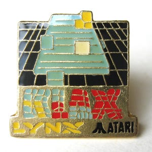 Könnte beinhalten: Ein Vintage Atari Lynx Anstecknadel mit einem geometrischen Design in Türkis, Gelb, Rot und Schwarz. Die Anstecknadel trägt die Wörter "LYNX" und "ATARI" in Gelb und Schwarz. Die Anstecknadel ist quadratisch mit einem goldenen Rand.