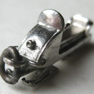 Może przedstawiać: Mały, srebrny charms w kształcie skutera śnieżnego z misternymi detalami. Charms posiada siedzenie, kierownicę i pętlę do przymocowania do naszyjnika lub bransoletki. Projekt skutera śnieżnego jest bardzo szczeg&oacute;łowy, z widocznymi gąsienicami i teksturowaną powierzchnią.